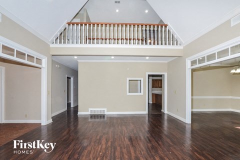 A spacious room with wooden floors and a staircase with white railings.