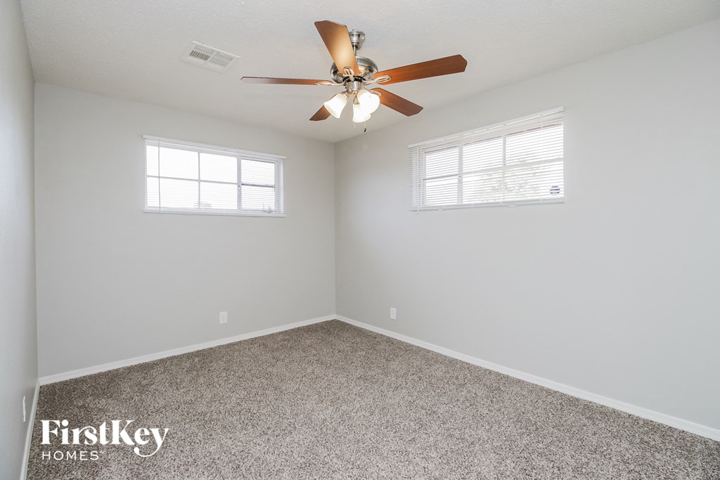 an empty room with a ceiling fan and two windows
