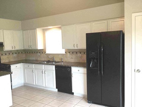 A black refrigerator sits in a kitchen with white cabinets.