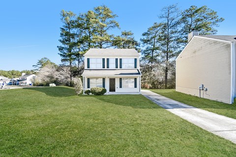 A house with a white exterior and a grey roof is surrounded by a green lawn.