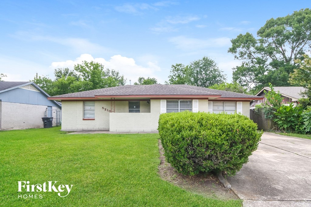 A house with a green lawn and a bush in front of it.