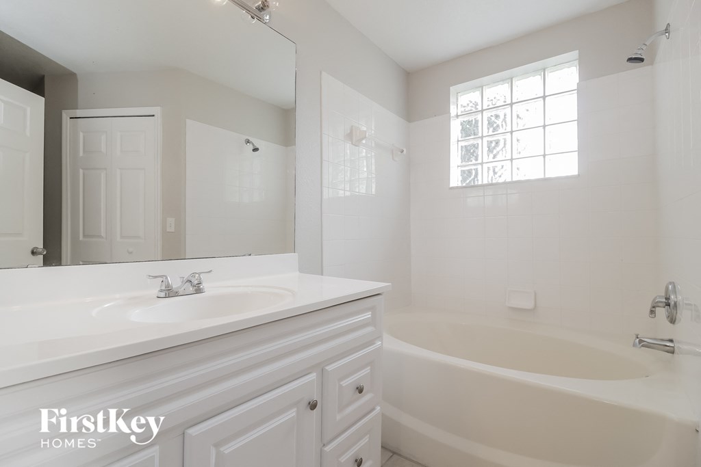 A white bathroom with a tub, sink, and mirror.