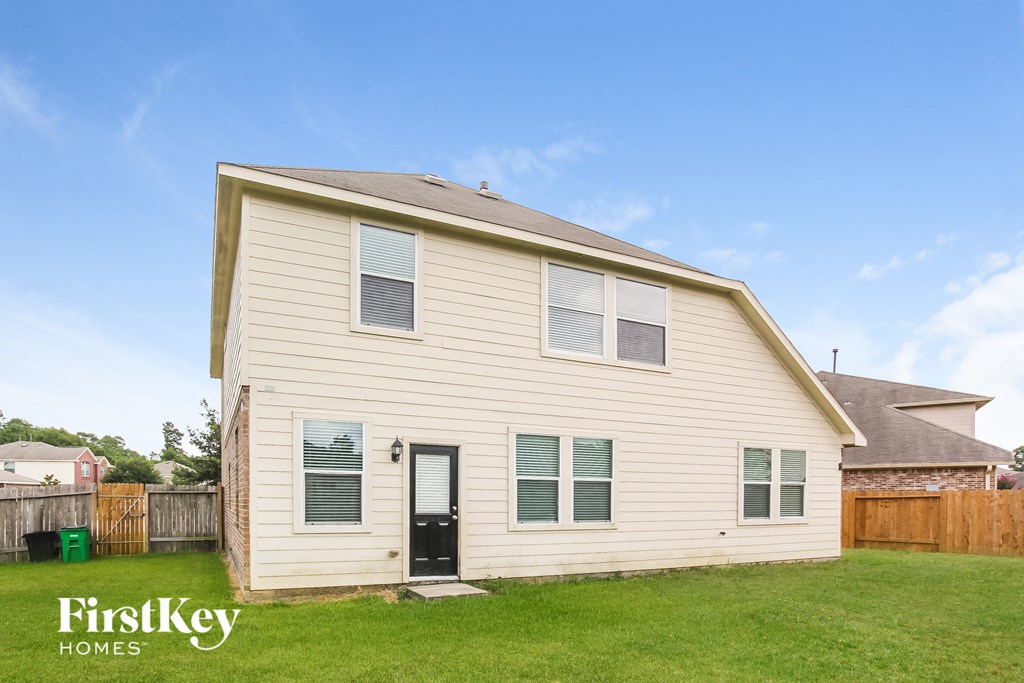 A house with a black door and a green trash can in front of it.