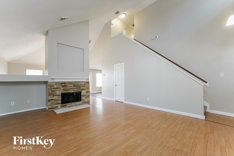 A spacious living room with a stone fireplace and wooden floors.