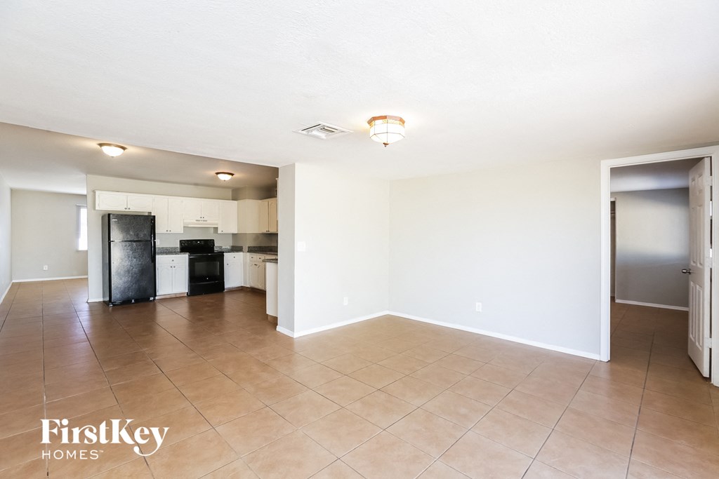 an empty living room and kitchen with white walls and tiled floors
