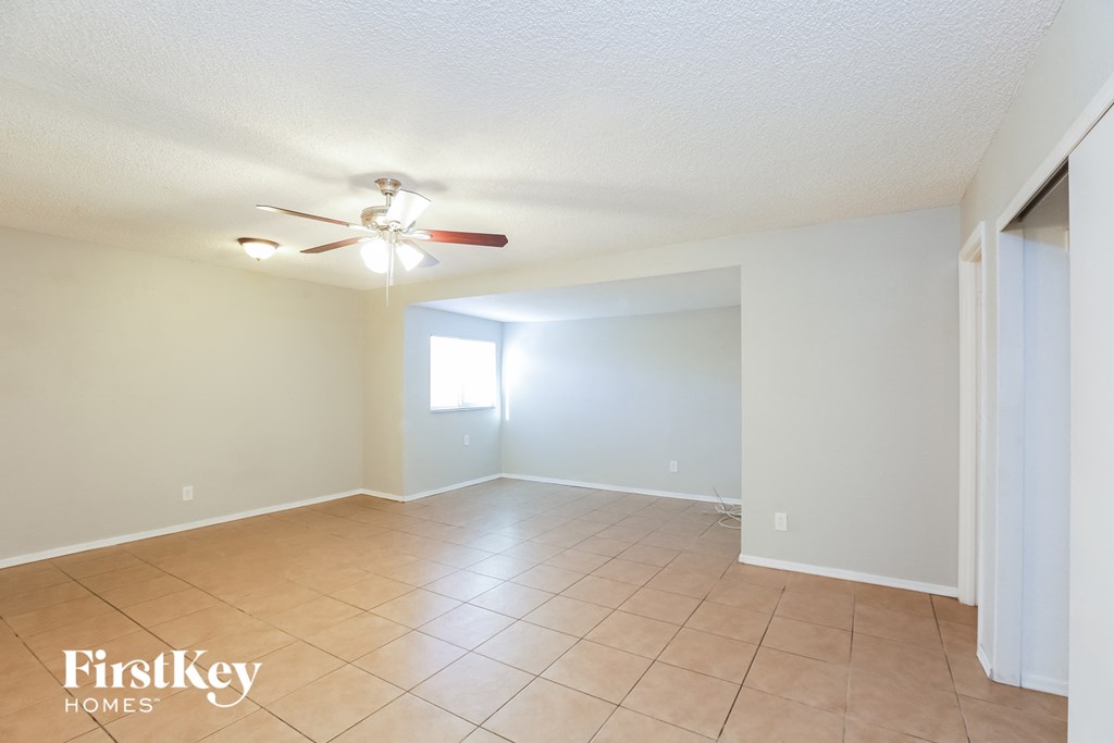 an empty living room with a ceiling fan and tiled floors