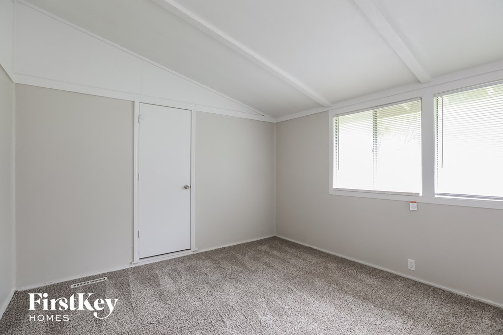 the bedroom of a home with white walls and carpet and two windows