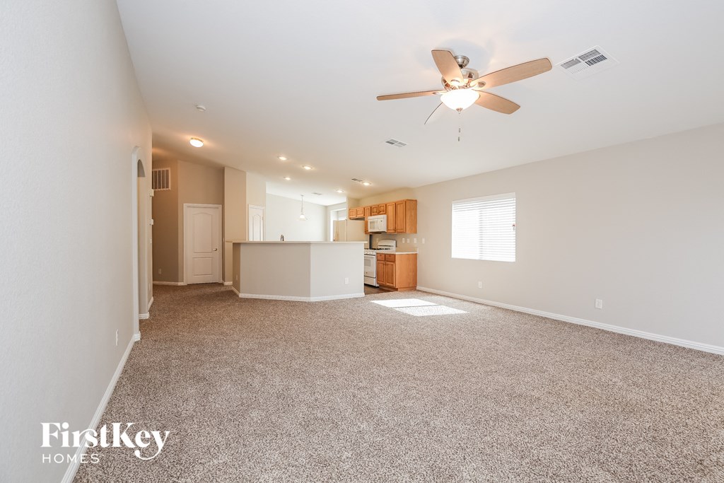 an empty living room with a ceiling fan and a kitchen