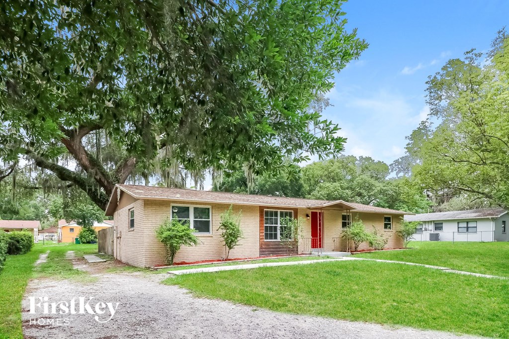 a small tan house with a red door and a tree