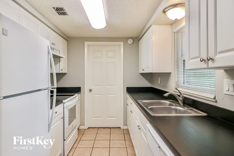 a kitchen with white cabinets and black counters and a white refrigerator and sink