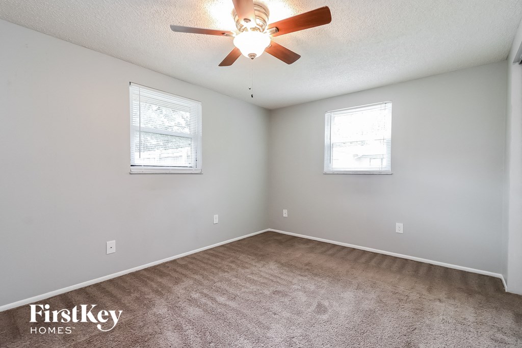 an empty room with a ceiling fan and two windows