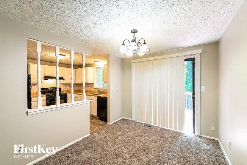an empty living room with a kitchen in the background