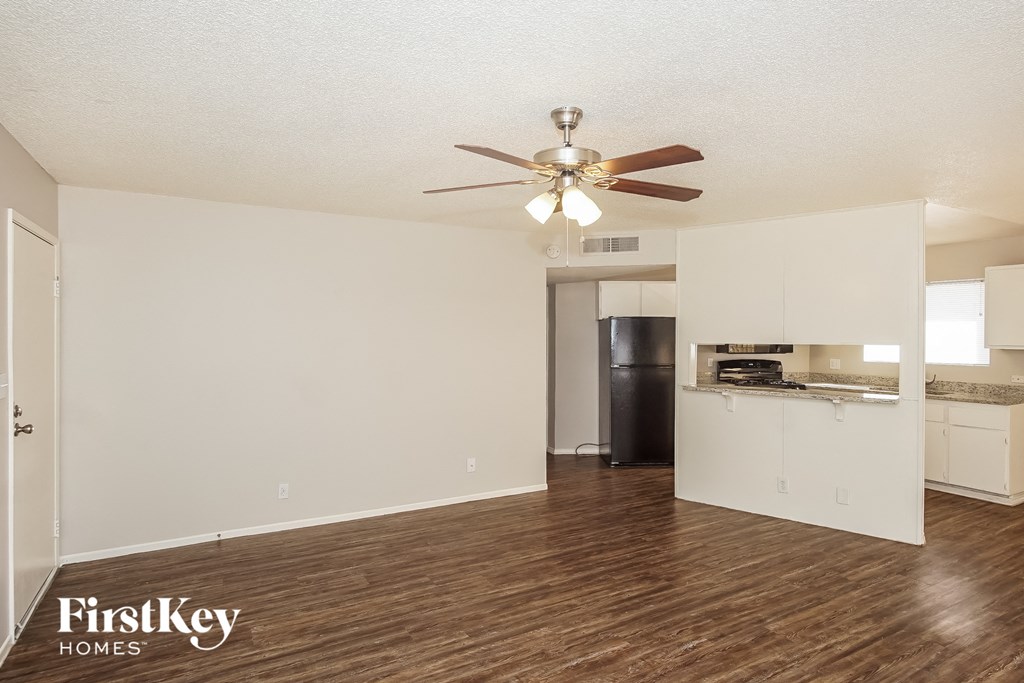 an empty living room with a ceiling fan and a kitchen