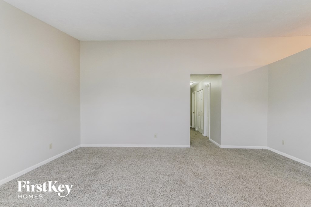 a bedroom with white walls and carpet and a hallway to a closet