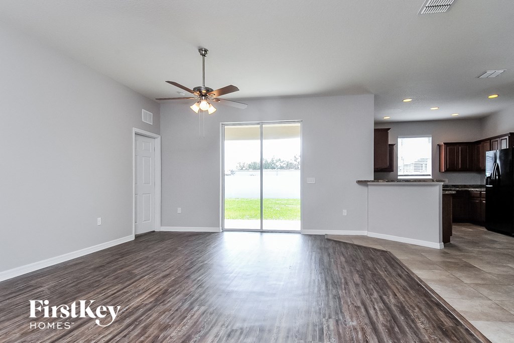 an empty living room with a kitchen and a ceiling fan