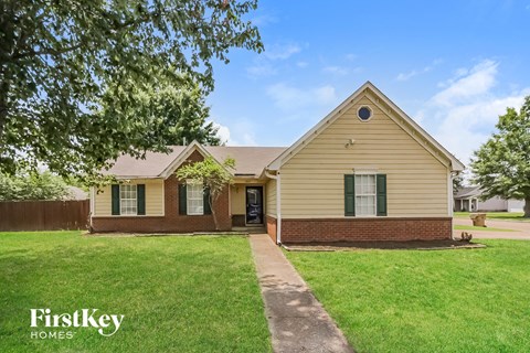 front view of a yellow house with green grass and trees