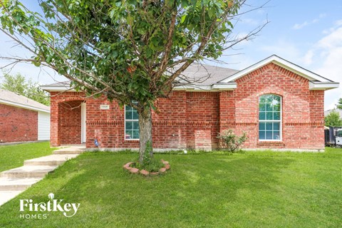 A red brick house with a tree in front and a white garage door.