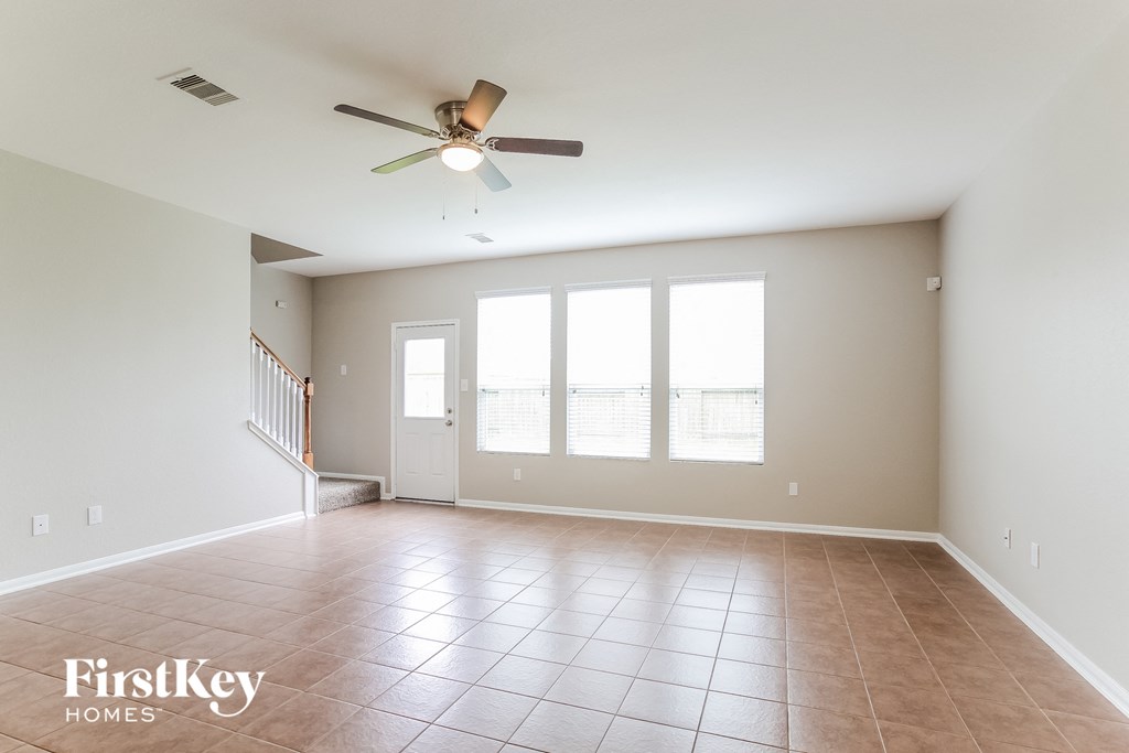 an empty living room with a ceiling fan and large windows