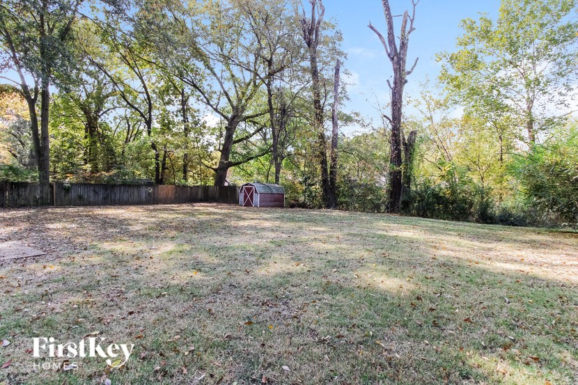 a large backyard with trees and a barbecue grill
