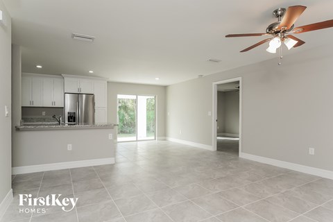 an empty living room with a kitchen and a ceiling fan