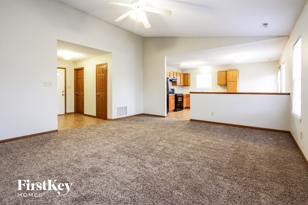 an empty living room with carpet and a kitchen