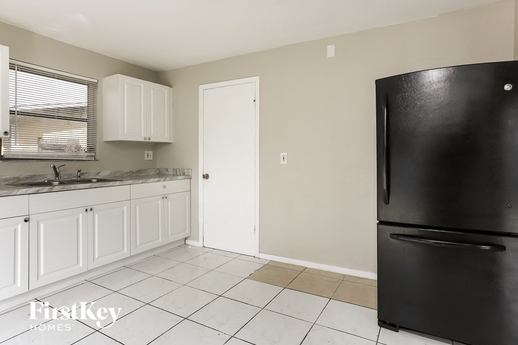 A black refrigerator in a kitchen with white cabinets.