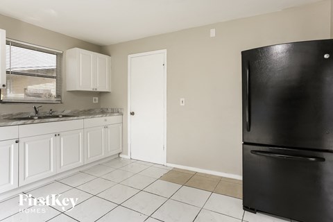 A black refrigerator in a kitchen with white cabinets.