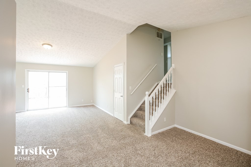 a white carpeted living room with a staircase and a white door