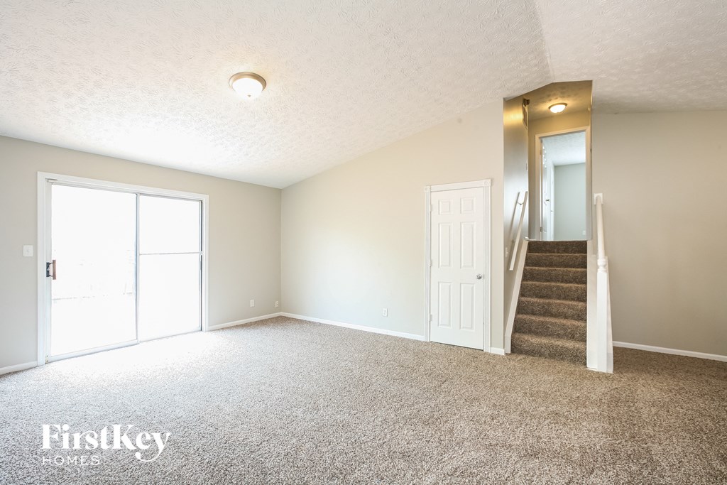 an empty living room with carpeted stairs and a white door