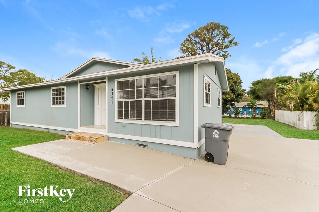 a blue house with a driveway and a trash can