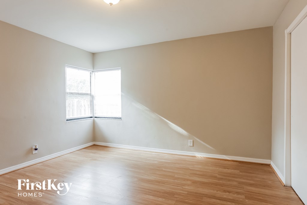 a bedroom with white walls and wood floors and a window