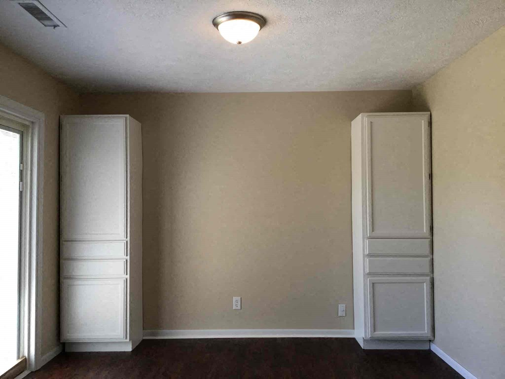 A room with two white cupboards and a window.