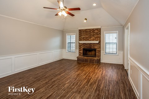 A spacious room with a brick fireplace and wooden flooring.