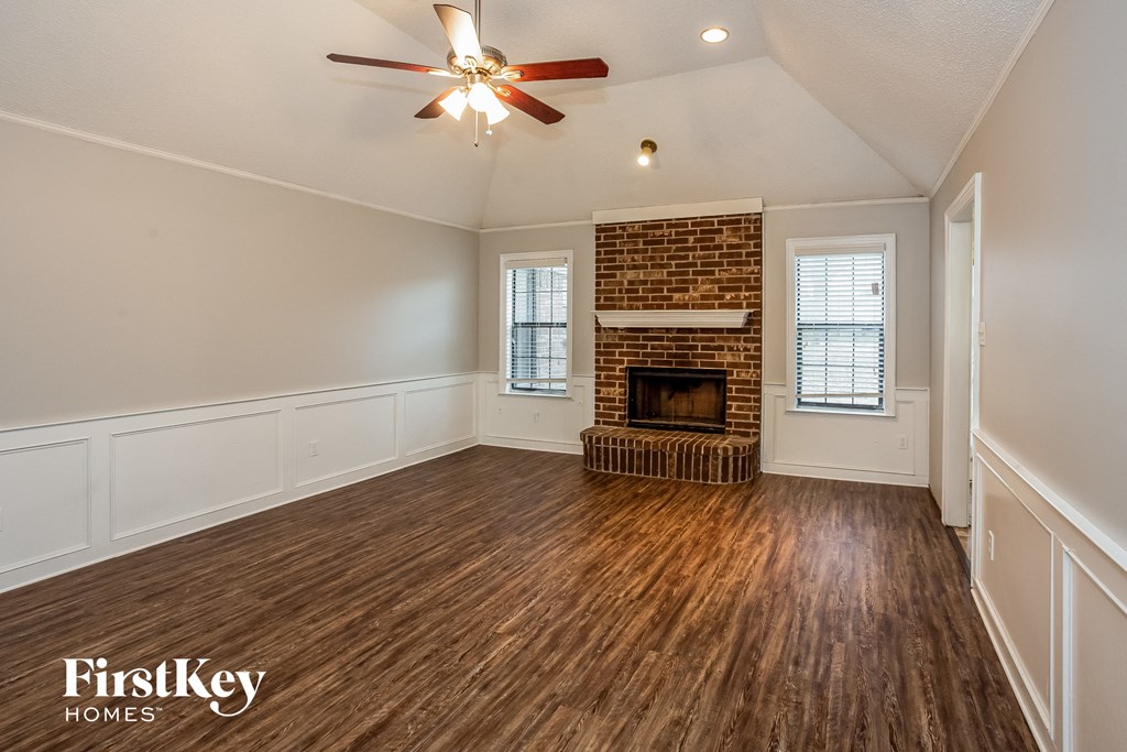A spacious room with a brick fireplace and wooden flooring.