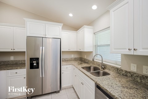 a white kitchen with granite counter tops and a stainless steel refrigerator