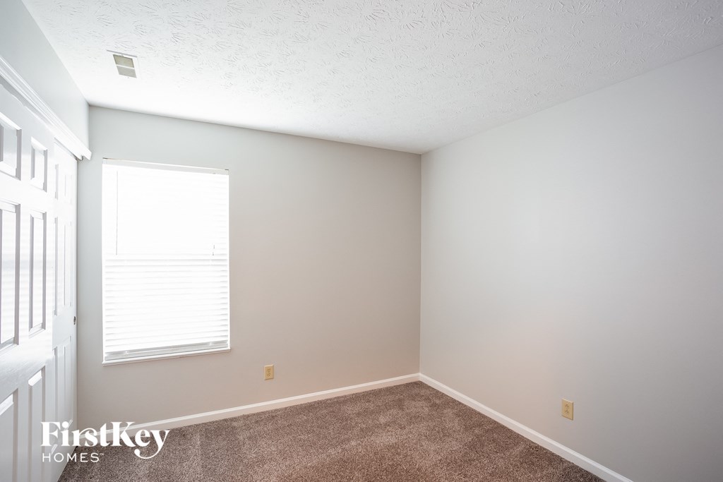 a bedroom with white walls and carpet and a window