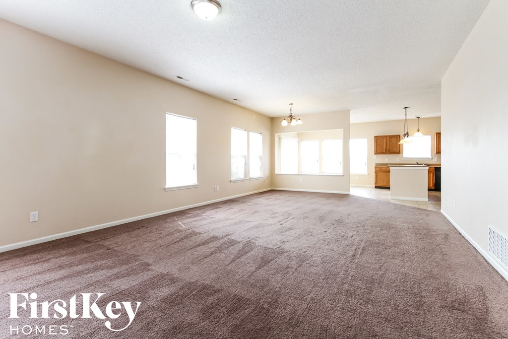 an empty living room with carpet and a kitchen