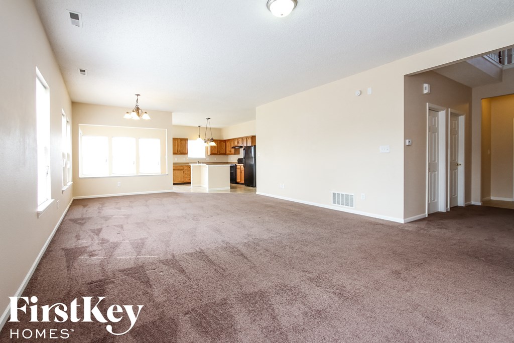 an empty living room with carpet and a kitchen
