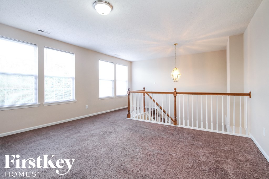 an empty living room with a staircase and three windows