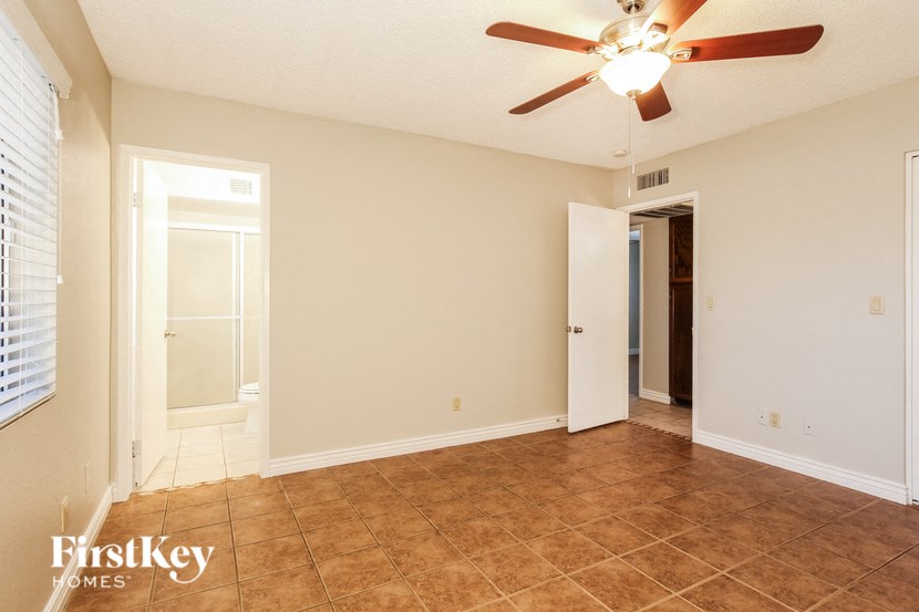 a empty living room with a ceiling fan and a door to a bathroom