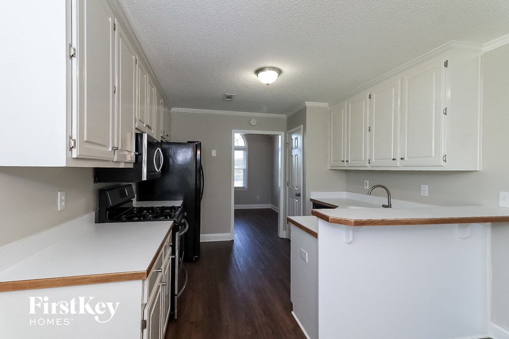 a renovated kitchen with white cabinets and black appliances and a hallway with a black refrigerator