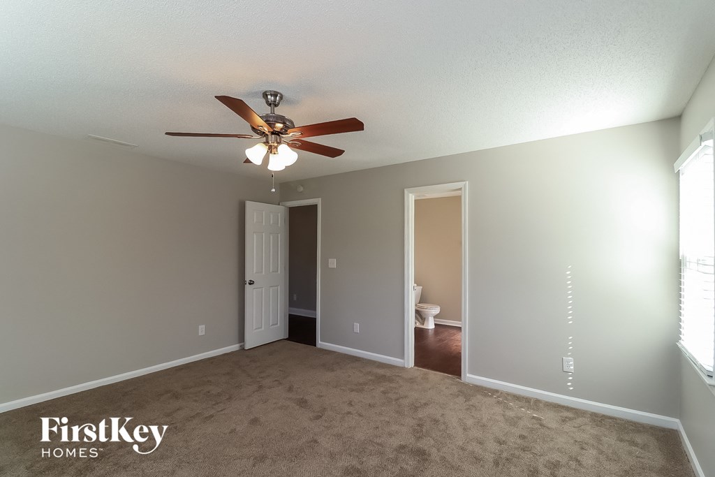 an empty living room with a ceiling fan and a door to the bathroom