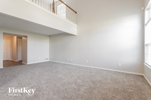 A spacious empty room with a carpeted floor and a staircase with a railing.