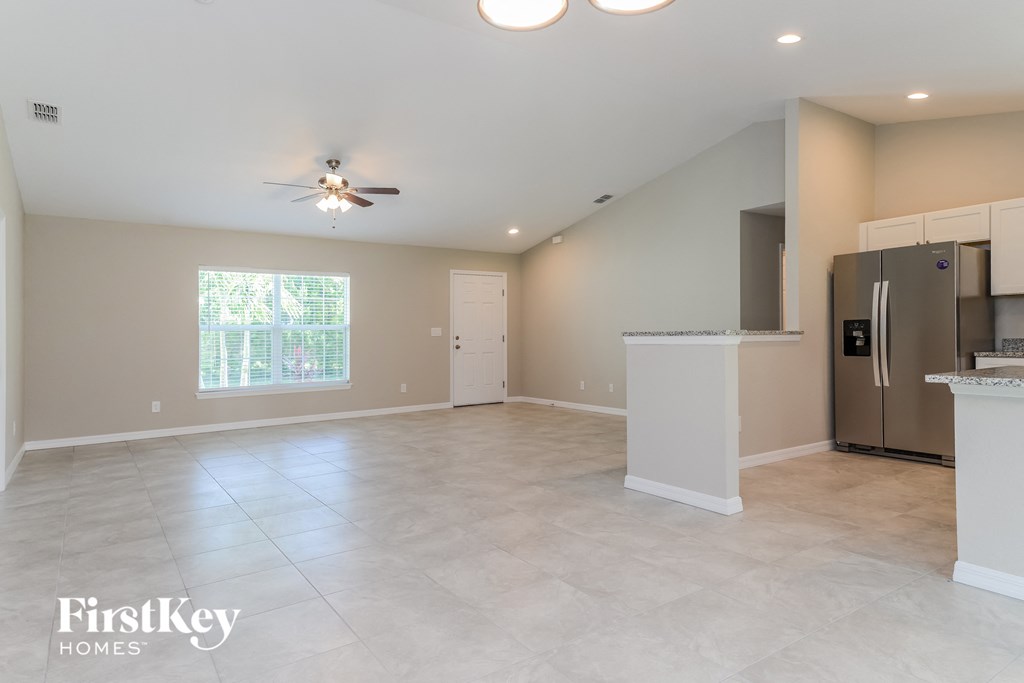 an empty kitchen and living room with a fridge and a ceiling fan