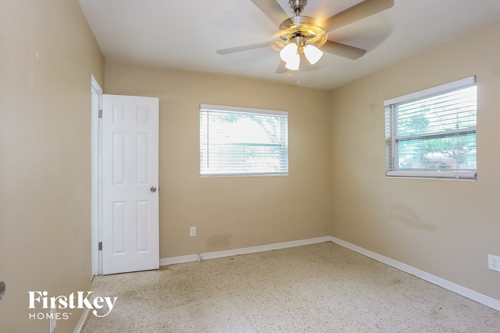 A room with a ceiling fan and two windows.