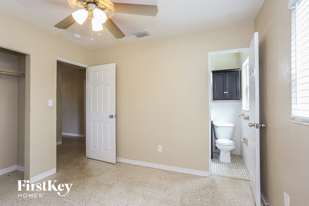 A room with a ceiling fan and a toilet in the bathroom.