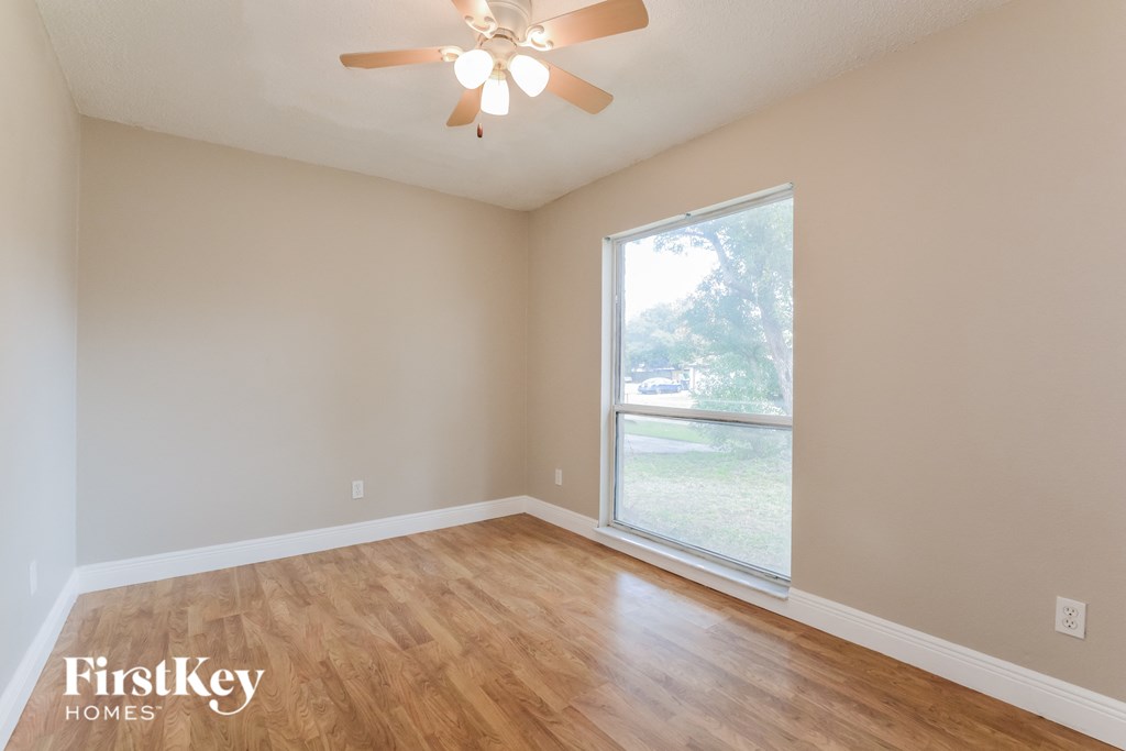 an empty living room with a large window and a ceiling fan