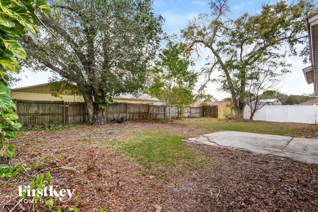 a backyard with trees and a fence and a sidewalk