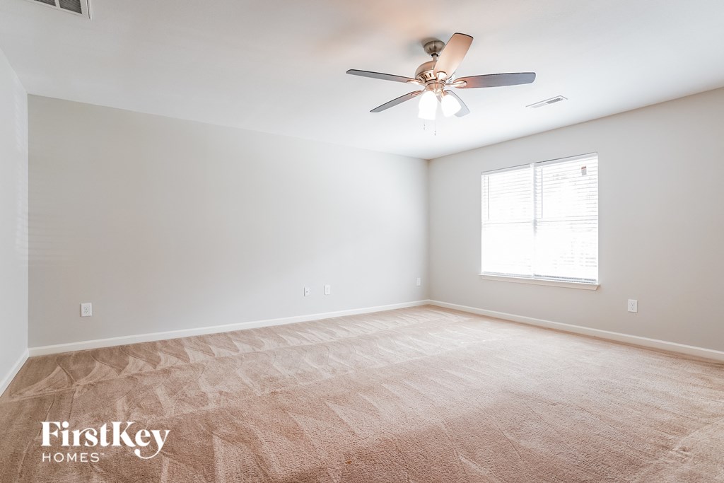 A room with a carpeted floor, a ceiling fan, and a window with blinds.