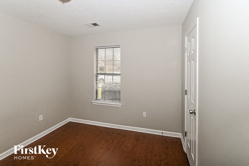 a bedroom with a window and wooden floors and a white door